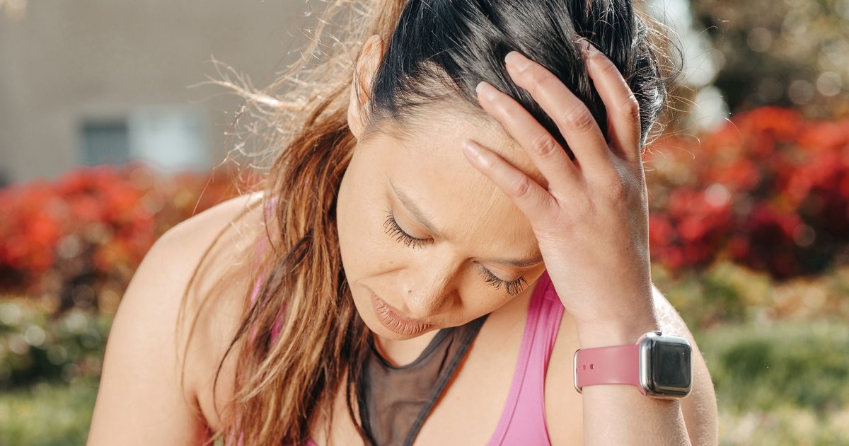 Mujer con ropa deportiva se toma la cabeza con gesto de cansancio y frustración después de entrenar